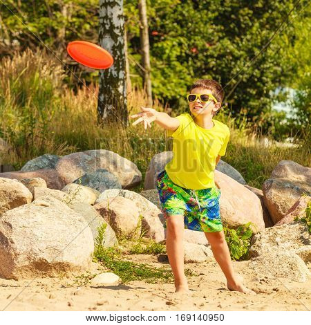 Play and fun concept. Little playful enjoyable boy kid throwing frisbee disc. Male child having fun playing outdoor on beach.