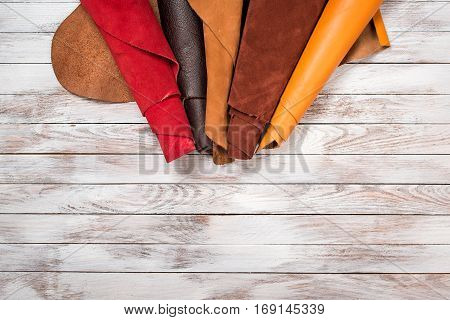 Brightly colored leather in rolls on the white wooden background. Leather craft. Copy space. Top view.