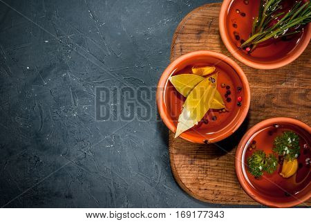 Selection of scented oils from herbs and spices: rosemary garlic pepper parsley bay leaf. On a cutting board on a dark gray stone kitchen table. Top view copy space