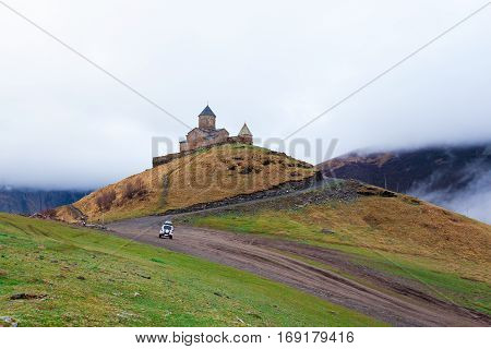 Gergeti Trinity Church Or Tsminda Sameba in the morning mist near village Stepantsminda, Georgia. Mount Kazbegi. Spring Or Summer Season.