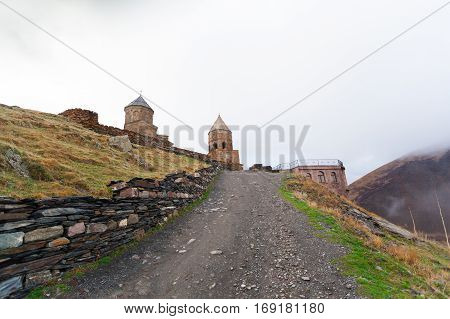 Gergeti Trinity Church Or Tsminda Sameba in the morning mist near village Stepantsminda, Georgia. Mount Kazbegi. Spring Or Summer Season.