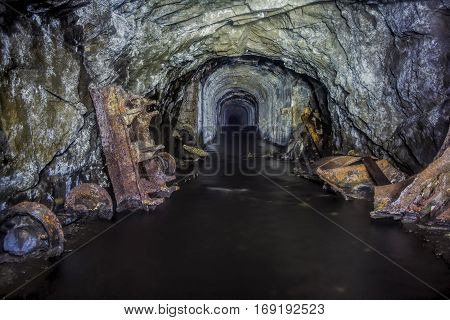 Flooded tunnel of an old abandoned coal mine with rusty remnants of trolleys