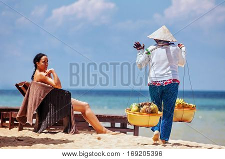 PHU QUOC, VIETNAM - APRIL 21, 2014: Vietnamese woman in traditional headdress, which protects from the sun offers fruits for sale to tourists at Long beach on Phu Quoc island, Vietnam. 