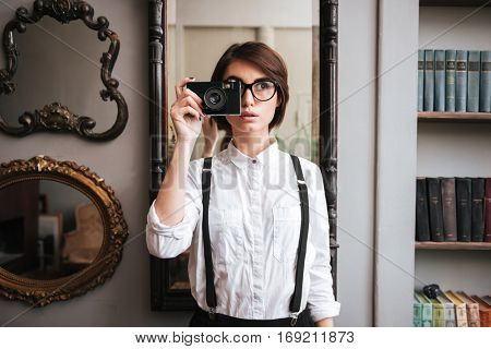 Authoress in glasses and white shirt making photo on retro camera