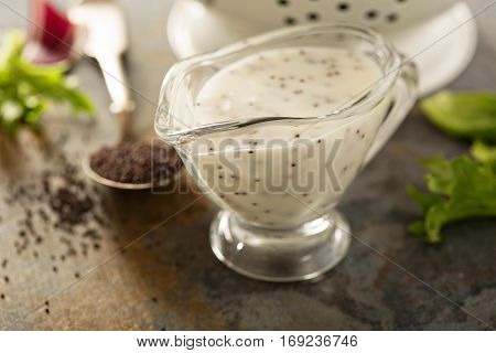 Poppy seed salad dressing or sauce in a glass dish with green salad leaves in the background