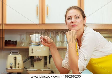 Pensive mature woman holding cup of coffee in kitchen. Housewife female with hot energizing beverage. Caffeine energy.