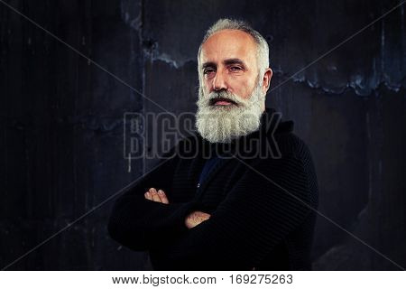 A mid shot of a man folding arms, standing against the black background, looking censoriously. Male having a serious look