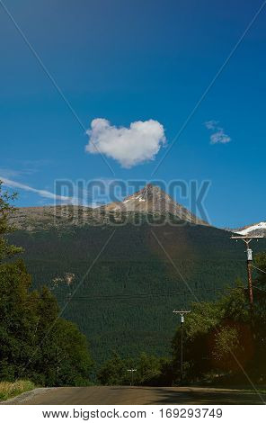 Heart shape cloud under mountain landscape. Road with cloud heart blue sky