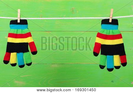 Striped colorful gloves hanging on the clothesline on green wooden background