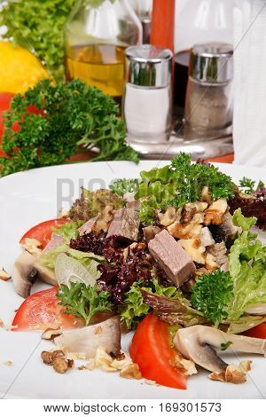 salad with ham mushrooms and nuts on a white plate with greens