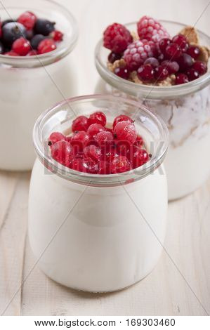 Homemade yogurt with frozen berries red currants black currants raspberries and cranberries in three banks