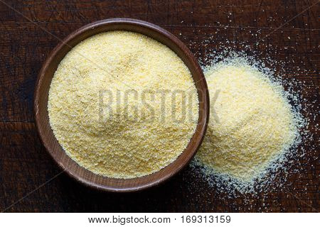 Cornmeal Polenta In Brown Wooden Bowl Isolated On Dark Wood From Above. Spilled Cornmeal.