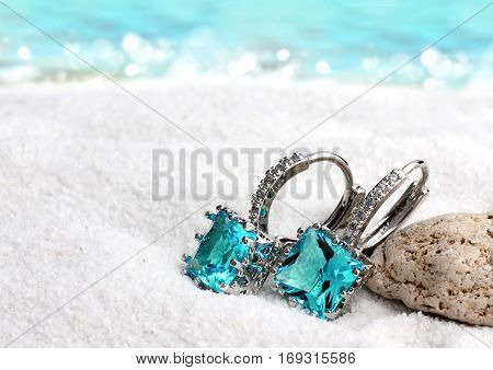 Jewelry earrings with aquamarine on sand beach background soft focus