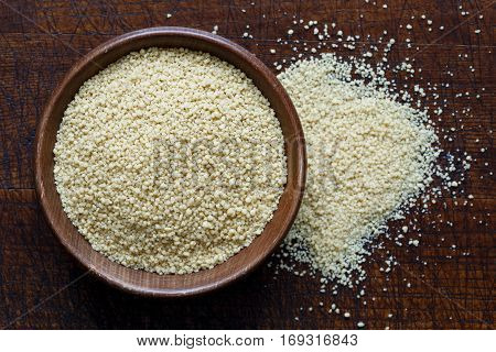 Dry Couscous In Brown Wooden Bowl Isolated On Dark Wood From Above. Spilled Couscous.