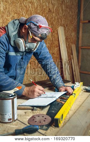 Man carpenter in his home studio working with wood and draws sketches in pencil in a notebook