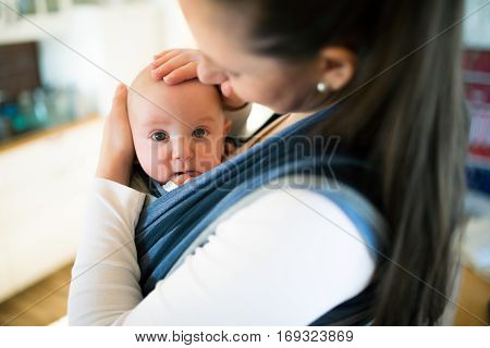 Beautiful young mother at home with her baby son in sling, stroking him gently