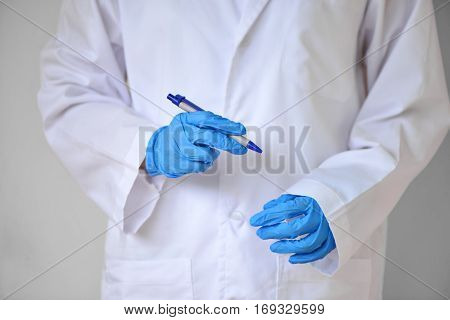 hand waering blue glove hold pen of scientist with lab coat standing at white wall