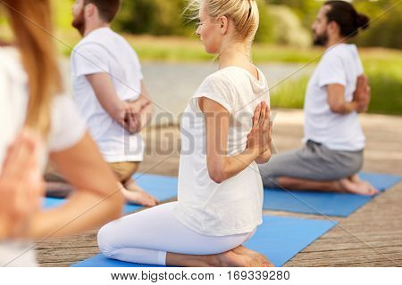 fitness, sport, yoga and healthy lifestyle concept - group of people exercising in reverse prayer pose on river or lake berth