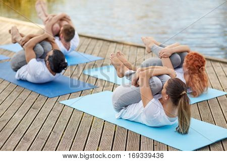 fitness, sport, yoga and healthy lifestyle concept - group of people making knee press pose on river or lake berth