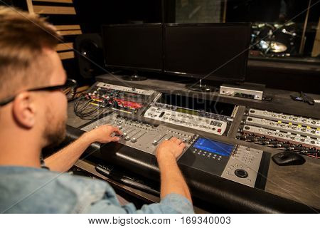 music, technology, people and equipment concept - man at mixing console in sound recording studio