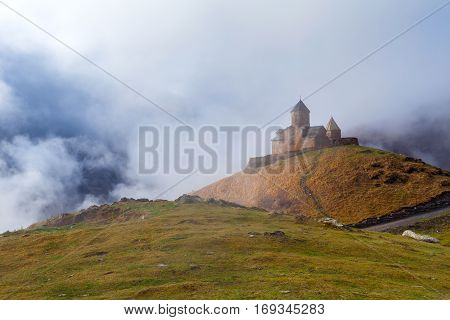 Gergeti Trinity Church Or Tsminda Sameba in the morning mist near village Stepantsminda, Georgia. Mount Kazbegi. Spring Or Summer Season.