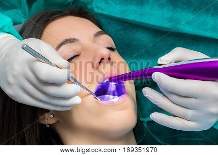 Macro close up of hand working on female teeth with blue led curing light.