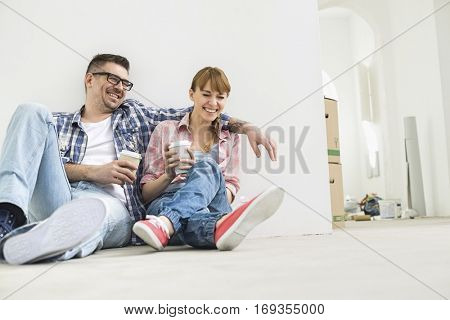 Full-length of cheerful couple with coffee cups in new house
