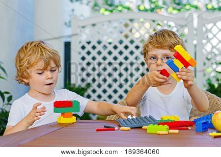Two little blond preschool kids boys playing with lots of colorful plastic blocks. Active children, brothers, friends and siblings having fun with building and creating together. Education, skills.