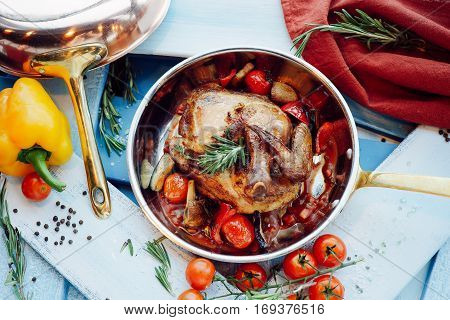 Chicken Tabaka in a pan with vegetables and tomatoes over blue wooden background