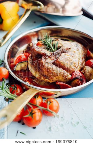 Chicken Tabaka in a pan with vegetables and tomatoes over blue wooden background