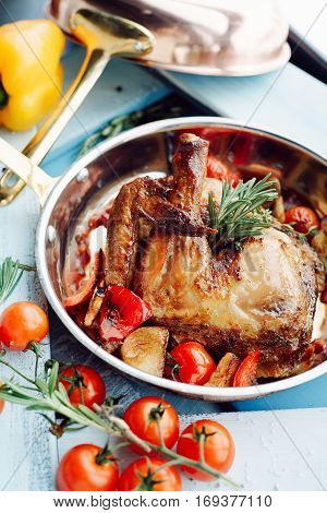 Chicken Tabaka in a pan with vegetables and tomatoes over blue wooden background