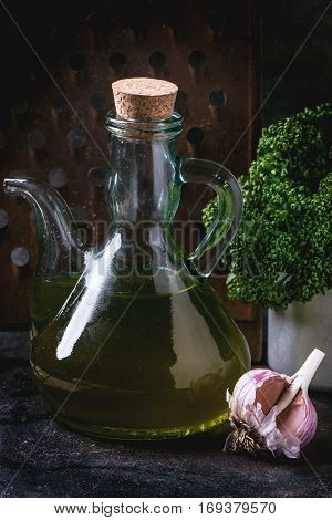 Glass bottle of olive oil with garlic and parsley over dark background