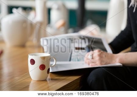 Woman with a big nice ring reading a magazine and drinking tea at a wooden table. Relaxing in a cafe and enjoying tea or coffee.