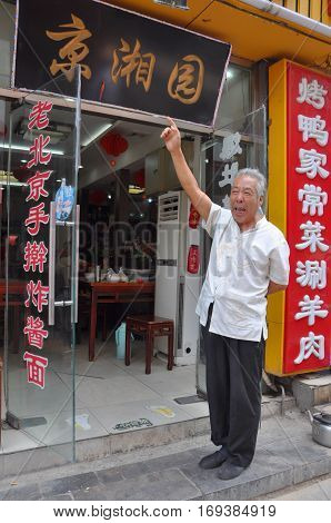 BEIJING, CHINA - JUN.24, 2012: An traditional old man is advertising in front of his restaurant. Photo taken in Qianmen Street, Beijing, China.