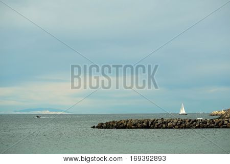 Beautiful sailing and motor boats float in calm blue sea water inshore along rocky coast outdoors on sunny summer day on sky background