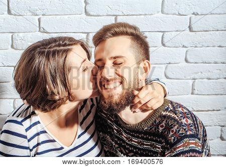 happy couple of pretty sexy woman or cute girl and handsome bearded man hipster in sweater kiss on brick wall background