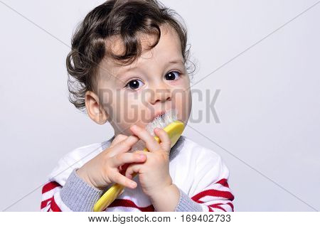 Portrait of a cute curly hair baby trying to comb his hair. Adorable one year old child being funny eating his hair brush.