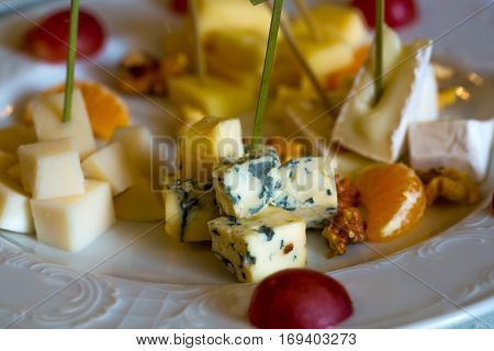 Delicious cheese plate with blue roquefort brie camambert gauda with garnishes grapes oranges and nuts on white porcelain background