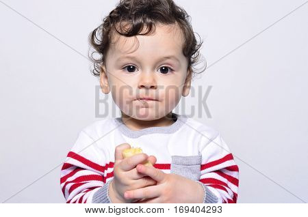 Portrait of a cute baby eating a banana.One year old kid eating fruits by himself. Adorable curly hair boy being hungry.