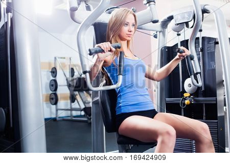 Pretty Caucasian smiling woman is working out on butterfly machine. Young Bodybuilder Doing Exercise For Chest In The Gym.