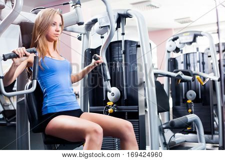 Pretty Caucasian smiling woman is working out on butterfly machine. Young Bodybuilder Doing Exercise For Chest In The Gym.