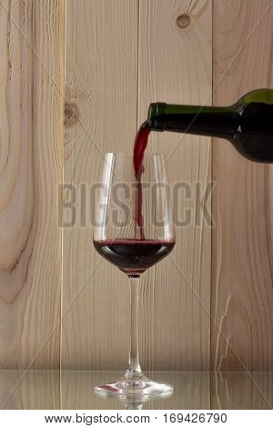 red wine being poured into a glass bottle of red wine with a brilliant glass on a wooden background on a glass stand