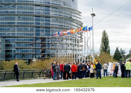 STRASBOURG FRANCE - OCT 7 2015: Rear view of tobacconists buralistes people protesting in front of the European Parliament building with flags placards while President Francois Hollande is entering the Parliament gates Confederation des buralistes