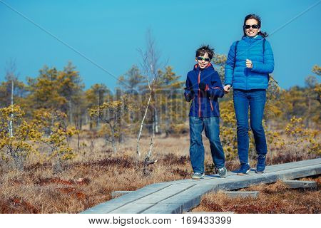 Cute little boy with his mother walking on trail in swamp and having fun, Kemeri national park, Latvia