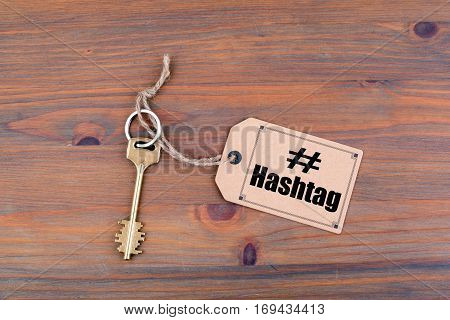 Key and a note on a wooden table with text: Hashtag.
