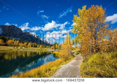 Canmore, near Banff Park. Path around the lake. The concept of hiking. Majestic mountains and autumn aspens reflected in the water
