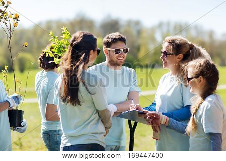 volunteering, charity, people and ecology concept - group of volunteers with clipboard planting trees in park
