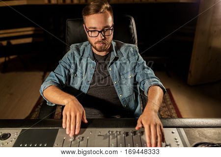 music, technology, people and equipment concept - man at mixing console in sound recording studio