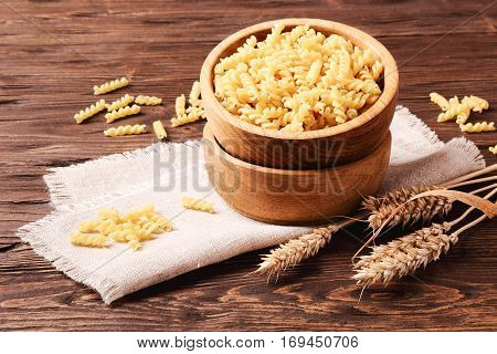 Raw pasta rotini and rye ears in a wooden bowl on the table