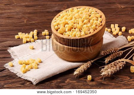 Raw pasta ditalini and rye ears in a wooden bowl on the table